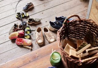 Mehrere Paare Schuhe und Sandalen liegen neben einem Korb mit Holz auf einem Holzboden in England.
