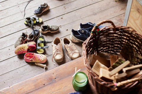 Diverse paia di scarpe e sandali su un pavimento di legno vicino a un cesto a Feather Down Chesters, UK.