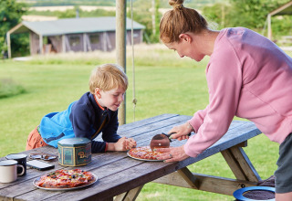 En kvinde skærer pizza til et barn ved et picnicbord på Feather Down East Shilvinghampton i Sydvestengland.