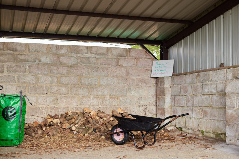 Overdekte houtschuur bij Feather Down East Shilvinghampton met kruiwagen, hout en een bord.