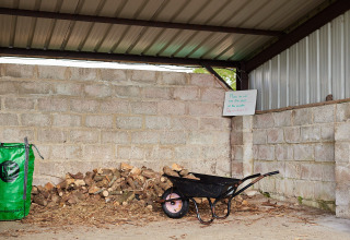 Überdachter Holzschuppen bei Feather Down East Shilvinghampton mit Schubkarre, Holz und Hinweisschild.