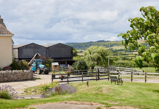 Uitzicht op Feather Down East Shilvinghampton vakantiepark met tractor, schuren en glooiende groene heuvels.