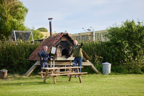 Dos hombres junto a una mesa de picnic y horno de leña en Feather Down East Shilvinghampton, Inglaterra.