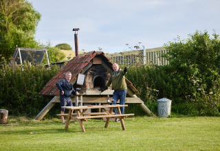 Zwei Männer stehen vor einem Holzofen und einem Picknicktisch im Feather Down East Shilvinghampton Park.