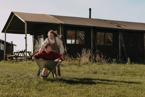 Due bambini giocano con una carriola davanti a una tenda safari a Feather Down Hoeve den Overdraght in Belgio.