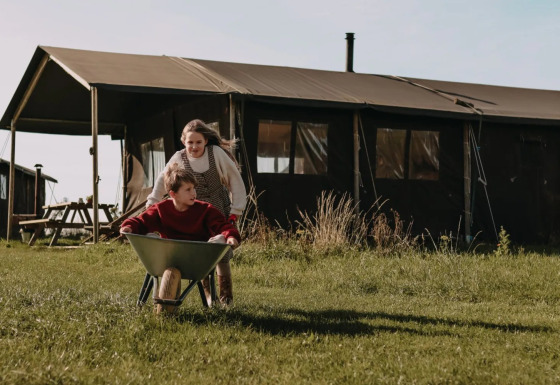 Two kids play with a wheelbarrow in front of a safari tent at Feather Down Hoeve den Overdraght in Belgium.