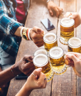 Des amis trinquent avec des bières à Weymouth, Angleterre, réunis autour d’une table en bois rustique au soleil.