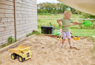 Young girl playing in a sandbox with a green shovel and toy dump trucks at Feather Down Heydon Grove Farm.