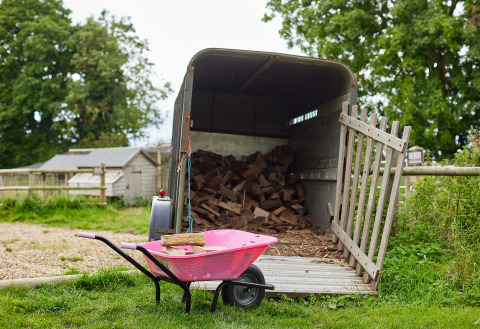 Roze kruiwagen voor een aanhanger vol brandhout op Feather Down Heydon Grove Farm, Engeland.