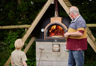 Volwassene en kind bij houtgestookte oven op Feather Down Heydon Grove Farm in Oost-Engeland.