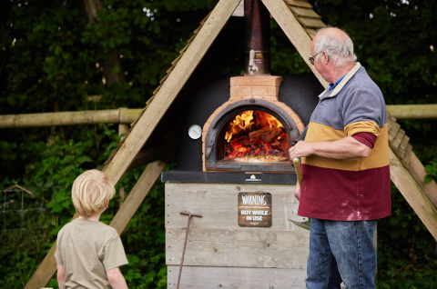 Ein Erwachsener und ein Kind stehen an einem Holzofen auf Feather Down Heydon Grove Farm in England.
