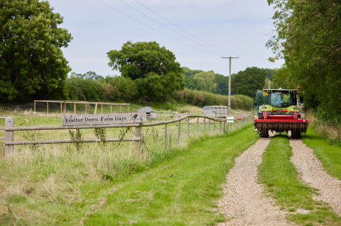 Traktor fährt auf Schotterweg bei Feather Down Farm Days, Heydon Grove Farm, Ferienpark in Ostengland.