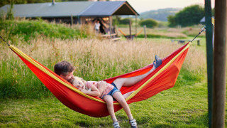 Padre e hija descansando juntos en una hamaca roja en Feather Down Warren Farm en el suroeste de Inglaterra.
