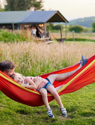 En far og datter slapper af i en rød hængekøje på Feather Down Warren Farm feriested i Sydvestengland.