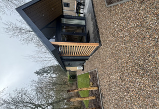 Moderna tiny house Tiny Loft al Veluwepark de Bosgraaf nei Paesi Bassi, con veranda in legno e vialetto di ghiaia.