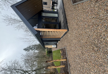 Moderne tiny house Tiny Loft ved Veluwepark de Bosgraaf i Holland med træterrasse og grusstier.