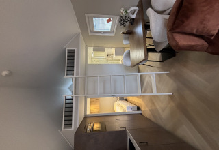 Indvendig udsigt over et tiny house i Veluwepark de Bosgraaf med hems, spisebord og kompakt køkken.