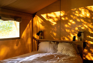 Interior of a safari tent at Rosenvold Strand Camping in Denmark, bed bathed in warm golden sunlight.
