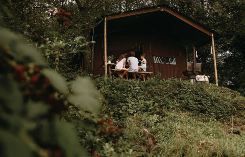 Una familia se sienta en una mesa de picnic fuera de una tienda safari rodeada de vegetación verde.