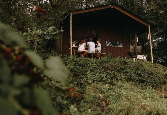 Una familia se sienta en una mesa de picnic fuera de una tienda safari rodeada de vegetación verde.