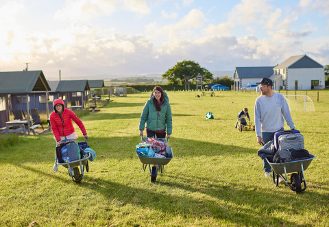 Tre persone trasportano bagagli con carriole a Feather Down Gwel Teg Farm, parco vacanze nel sud-ovest dell’Inghilterra.