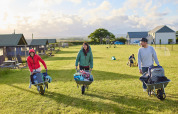 Tre personer transporterer bagage i trillebøre på Feather Down Gwel Teg Farm feriepark i det sydvestlige England.