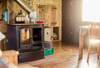 La luce del sole illumina una cucina rustica presso Feather Down Gwel Teg Farm, con stufa a legna e pavimento in legno.