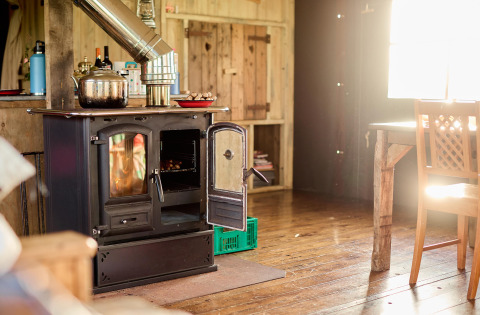 Sunlight shines into a rustic kitchen at Feather Down Gwel Teg Farm, featuring a wood-burning stove and wooden floor.