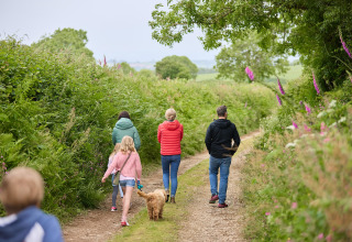 Familie og børn går med hund på en naturskøn sti omgivet af grønne planter ved Feather Down Gwel Teg Farm.