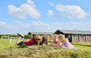 Kinder spielen und lachen auf einem Hügel vor Zelten und Fußballtoren im Feather Down Gwel Teg Farm Ferienpark.