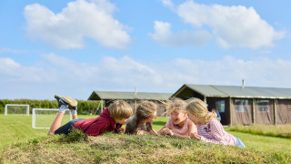Kinderen lachen en spelen op een grasheuvel bij Feather Down Gwel Teg Farm, vakantiepark in Zuidwest-Engeland.