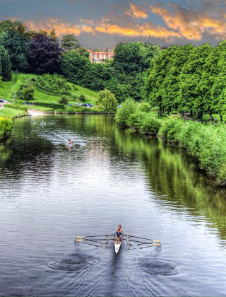 Roeer på flod omgivet af grønne træer og hytter nær Shrewsbury, Wales, ved solnedgangens skær.