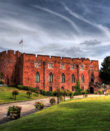 Et storslået slot bygget af rød mursten set under dramatiske skyer nær Shrewsbury, Wales, Storbritannien.