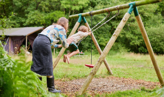 En voksen skubber et barn på en gynge i det grønne ved Feather Down Upper Shadymoor Farm i Wales, Storbritannien.