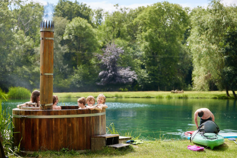 Børn nyder en træ-hot tub ved søen, mens en mand gør en kajak klar ved Feather Down Upper Shadymoor Farm.
