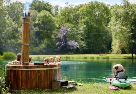 Børn nyder en træ-hot tub ved søen, mens en mand gør en kajak klar ved Feather Down Upper Shadymoor Farm.