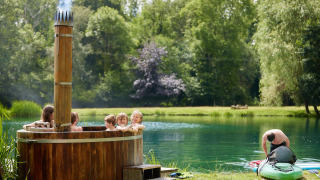 Børn nyder en træ-hot tub ved søen, mens en mand gør en kajak klar ved Feather Down Upper Shadymoor Farm.