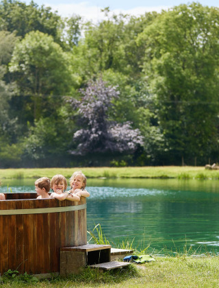 Børn nyder en træ-hot tub ved søen, mens en mand gør en kajak klar ved Feather Down Upper Shadymoor Farm.