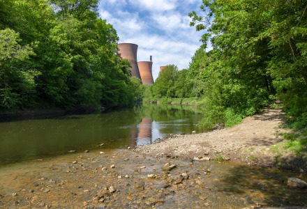 Naturligt landskab nær Shrewsbury i Wales med grønne træer, en stille flod og kraftværkets tårne i baggrunden.