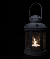 Farol negro con una vela encendida en su interior, fotografiado en la oscuridad en un parque glamping.