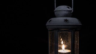 Farol negro con una vela encendida en su interior, fotografiado en la oscuridad en un parque glamping.