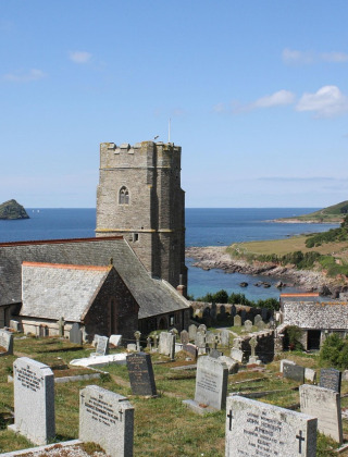 Foto de una iglesia junto al mar con cementerio en primer plano y acantilados bajo un cielo azul brillante.