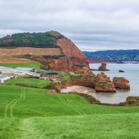 Paisaje cerca de Kingswear, suroeste de Inglaterra, con verdes campos, acantilados rojizos y casas junto al mar.