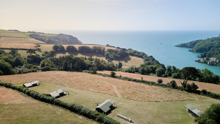 Aerial view of Feather Down Fountain Violet Farm holiday park with tents, fields, and sea in South West England.