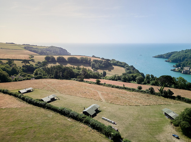 Luchtfoto van Feather Down Fountain Violet Farm vakantiepark met tenten, weilanden en zee in Zuidwest-Engeland.