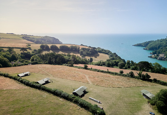 Luchtfoto van Feather Down Fountain Violet Farm vakantiepark met tenten, weilanden en zee in Zuidwest-Engeland.