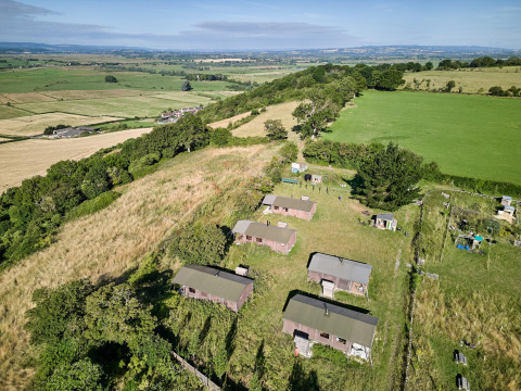 Vista aérea de Feather Down Glastonbury Hill Farm, parque vacacional con cabañas y campos en el suroeste de Inglaterra.