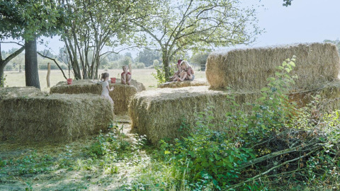 Kinderen spelen op hooibalen onder bomen in Feather Down La Ferme de Fontenille, Canarische Eilanden.