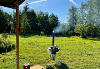 Udendørs picnicbord med rødt service, blomster og udsigt til en grøn græsplæne og træer i solskin.