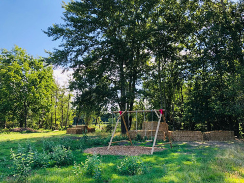 Buitenspeelplaats met houten schommel en strobalen omringd door bomen bij La Ferme de Fontenille.